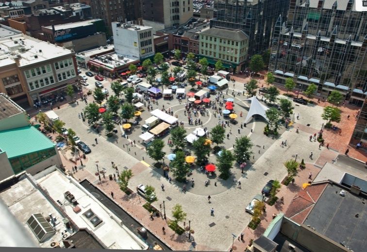 Överblick över ett centralt torg med människor, träd och marknadsstånd